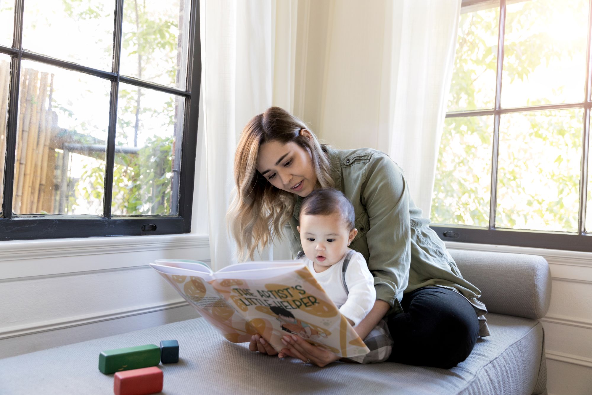 A young mom reads a book to her attentive baby, possibly representing parenting or being pregnant with a substance use disorder