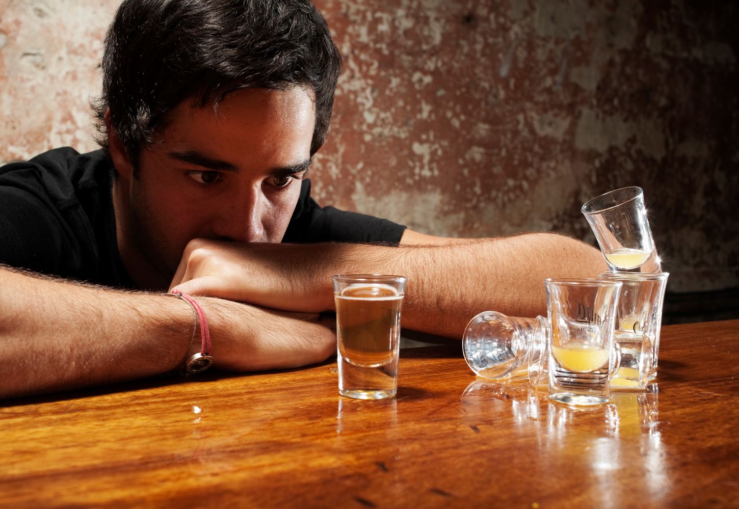 A young man stares at drinks on a bar, representing signs your college student is drinking too much