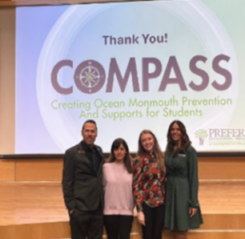 Linda, Cori, and others posing in front of the COMPASS conference screen